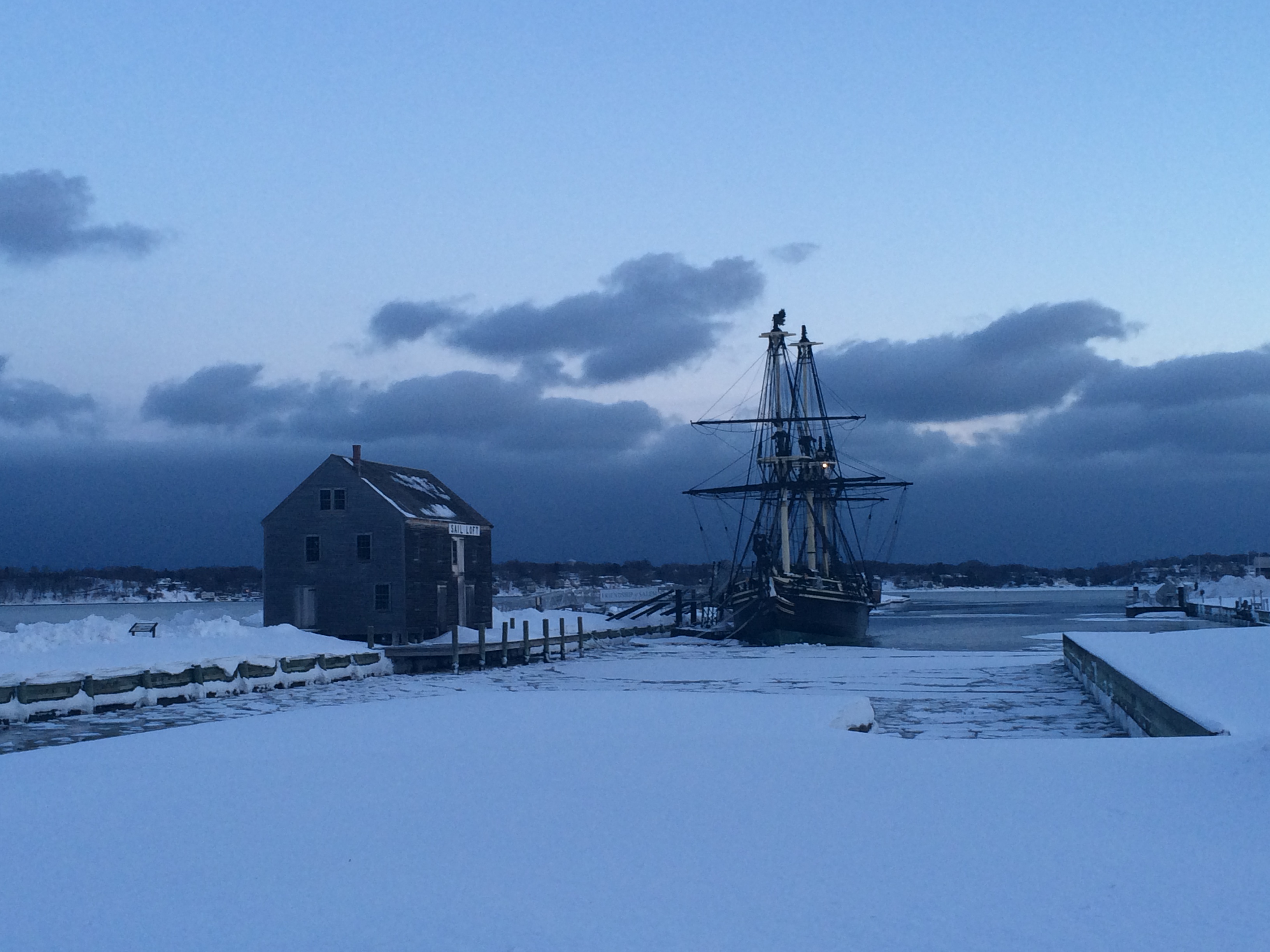The friendship of salem docked at dusk in the winter, snow coats the ground and floats on the water