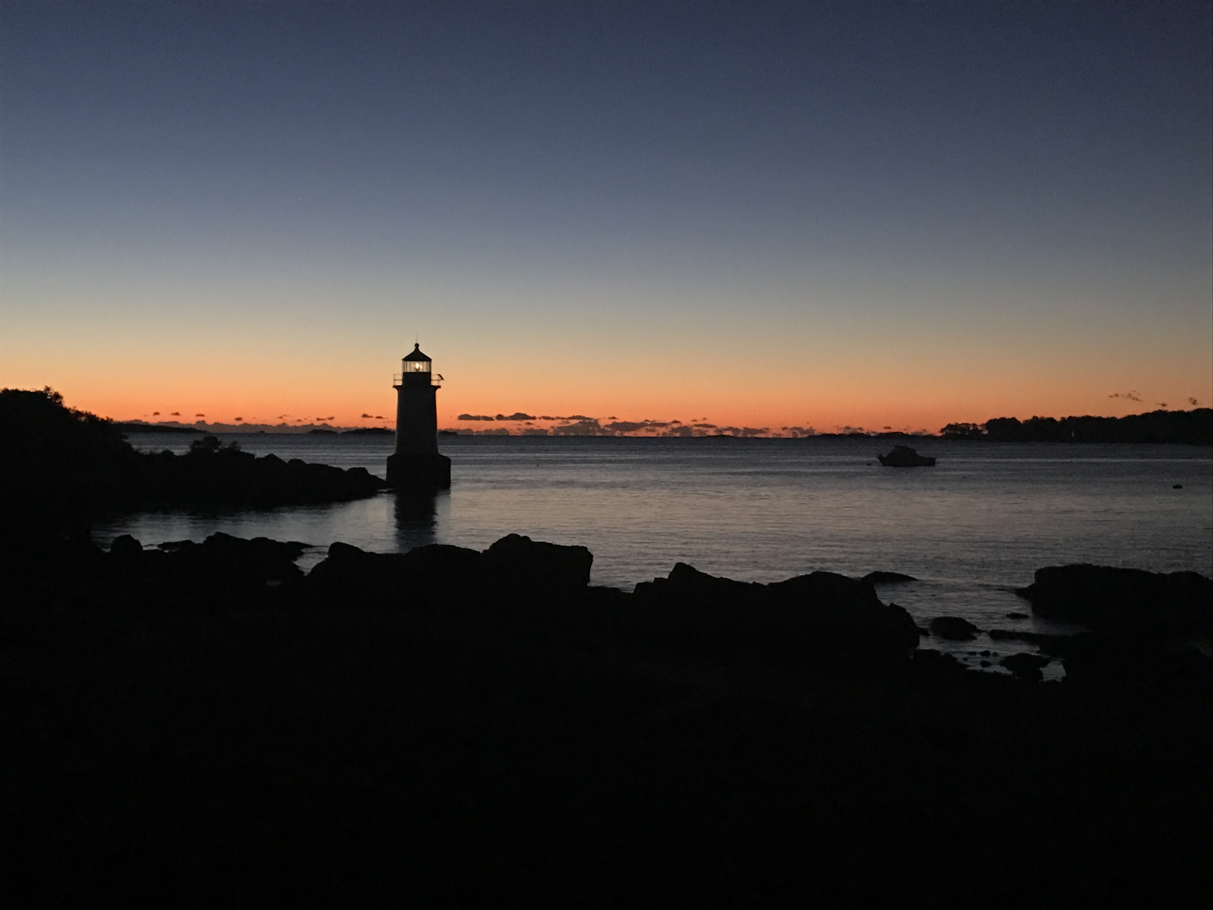 The silouette of the shore line and the winter island light house against a blue orange sunset and the ocean water