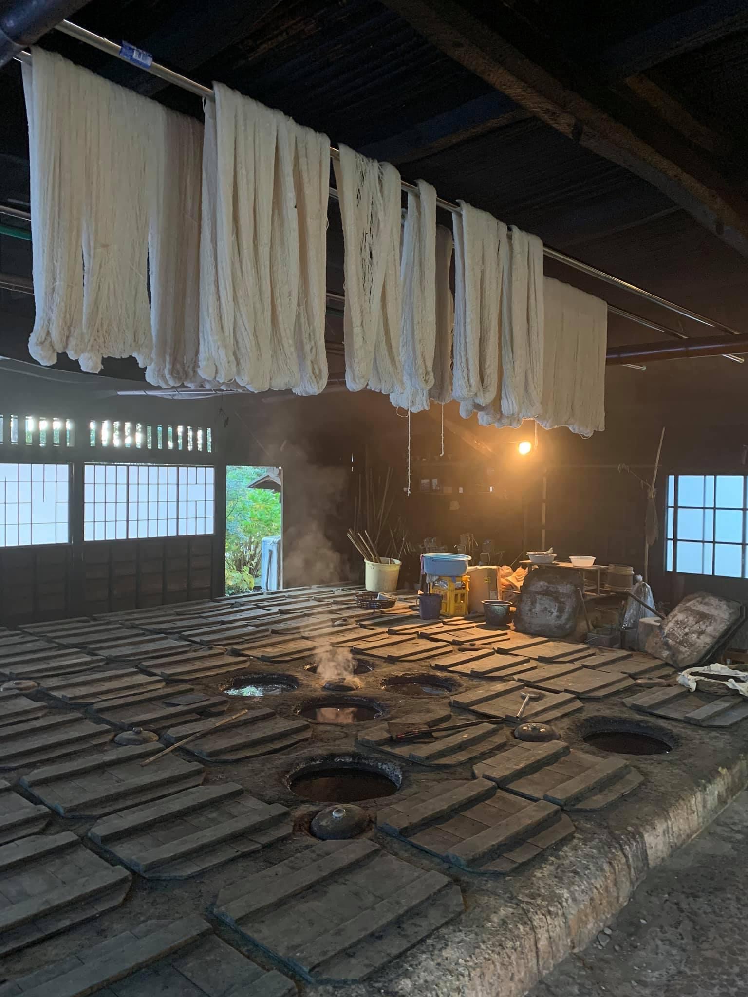 A room in which traditional indigo is being mad, in stone pits in the floor, with wooden covers. White linen thread hangs from the ceiling ready for dying